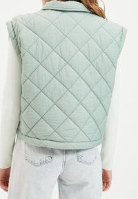 Miętowa pikowana kamizelka z diamentowym przeszyciem, z kołnierzykiem i bez rękawów, w połączeniu z jasnymi dżinsami.