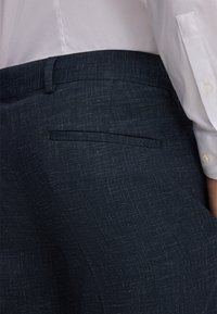 Donkerblauwe op maat gemaakte broek van textuurstof, met een achterzak en een gladde tailleband, gecombineerd met een witte blouse met kraag.