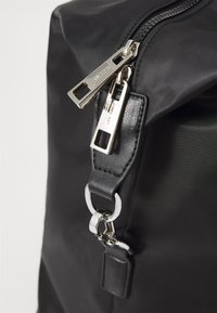 Borsa in nylon nera con cerniera e parti metalliche argentate, attacco per tracolla in pelle e cuciture dettagliate sui bordi.