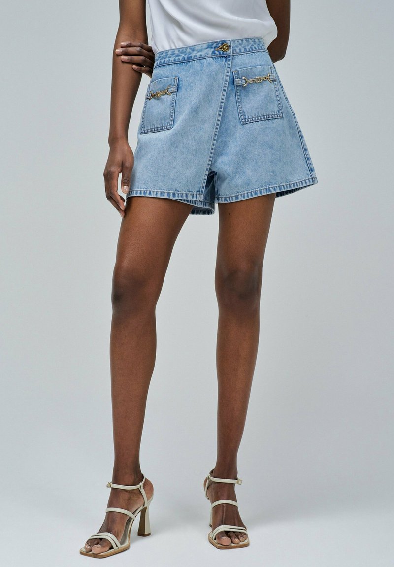 Shorts de mezclilla azul claro con cintura alta, dos bolsillos frontales adornados con acentos de cadena dorada y cierre de cremallera.