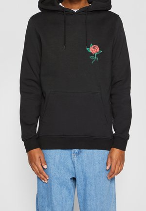 Haut en coton noir avec poche kangourou, ornée d'une broderie de rose rose et de feuilles vertes sur la partie gauche de la poitrine. Capuche avec cordon ajustable.