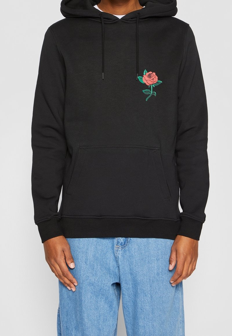 Haut en coton noir avec poche kangourou, ornée d'une broderie de rose rose et de feuilles vertes sur la partie gauche de la poitrine. Capuche avec cordon ajustable.