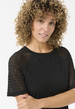 Haut noir avec un tissu côtelé et des manches texturées en dentelle. Encolure ronde, manches courtes et silhouette ajustée.