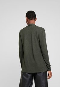 Dunkelgrüner, langärmliger Strickpullover mit strukturierter Oberfläche und gerippten Bündchen, kombiniert mit schwarzen Lederhosen. Einfaches, figurbetontes Design.
