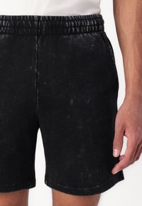 Shorts en denim noir avec une texture délavée, une taille élastique et des coutures latérales. Les jambes sont ourlées sans détails supplémentaires.