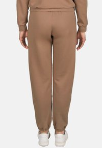 Bruine joggers met elastische tailleband en taps toelopende boorden, gemaakt van zacht materiaal. Draag ze met witte sneakers voor een ontspannen pasvorm en een eenvoudig ontwerp.