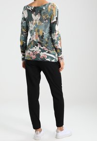 Blommönstrad stickad tröja i teal, med långa ärmar och en vid halsringning, tillsammans med svarta smala byxor och vita sneakers.