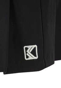 Černý tkaninový oděv s plisovaným designem, s čtvercovým bílým vyšívaným logem po straně. Měkká textura, minimalistický styl.