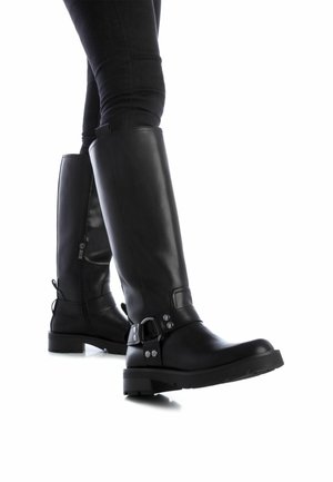 Botas de cuero negro hasta la rodilla con puntera redonda, cremallera lateral, hebilla metálica decorativa y suela de goma texturizada. Costuras detalladas presentes.