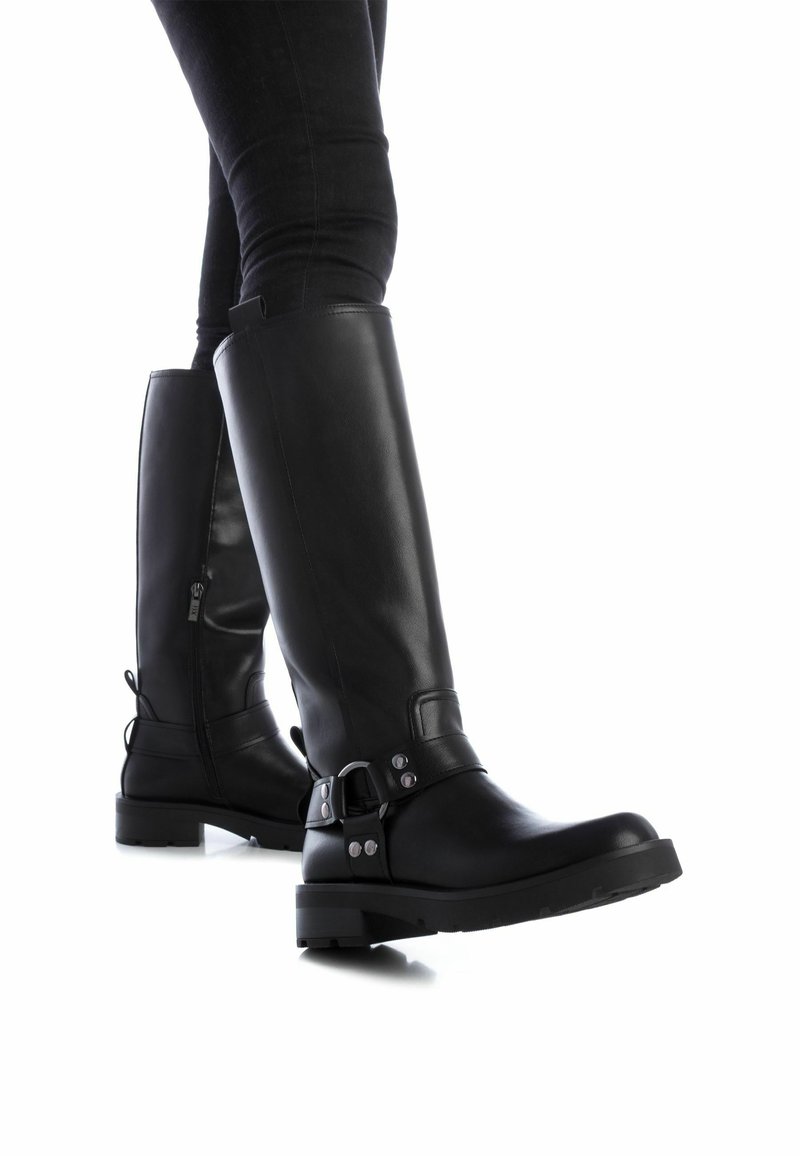 Botas de cuero negro hasta la rodilla con puntera redonda, cremallera lateral, hebilla metálica decorativa y suela de goma texturizada. Costuras detalladas presentes.