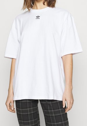 Camiseta de algodón blanca y oversized con mangas cortas y cuello redondo. Presenta un pequeño logotipo negro de Adidas en el pecho. Sin patrones.