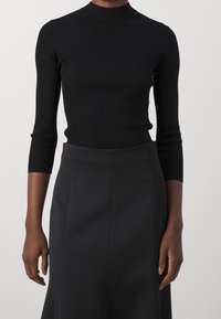 Top negro de manga larga con textura de canalé y cuello alto, combinado con una falda negra de textura suave y líneas limpias.