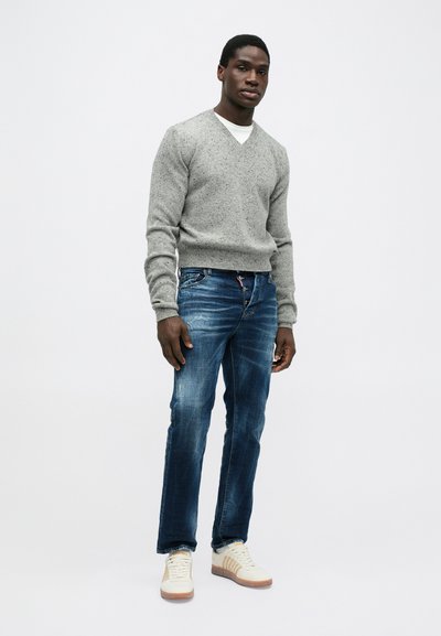 Grijze v-hals trui met textuur breiwerk, blauwe denim jeans met een vervaagde afwerking, en witte sneakers met bruine accenten en gestreepte details.