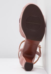 Vue de dessous d'une chaussure à talon haut en daim rose avec une semelle en caoutchouc montrant une texture côtelée et le nom de la marque "Chie Mihara."