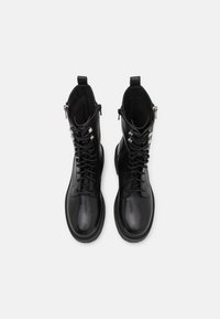 Botas de cuero negras hasta el tobillo con un acabado suave, punta redondeada, diseño con cordones y cremalleras laterales para facilitar su uso. Forro interior texturizado.