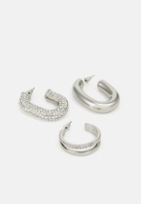 Trois paires de boucles d'oreilles créoles : une couverte de strass transparents, une en argent lisse et une avec une subtile rayure de strass.