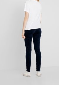 Marina blå sammetsbyxor med slim fit och subtil struktur, kombinerat med en vit t-shirt med kort ärm och vita sneakers, sedd bakifrån.