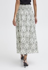 Maxi krilo v beli barvi z zapletenimi zelenimi paisley vzorci, elastičen pas, lahek material in kombinirano s črnimi sandali na peto.