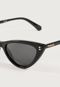 Čierne slnečné okuliare v štýle mačacích očí s tmavými šošovkami a zlatým brandingom na spánku a prednom rohu.