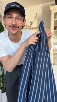 Marineblaues gestreiftes Hemd mit hellblauen Streifen, kurzen Ärmeln und einem Kragen. Der Stoff wirkt weich und leicht.