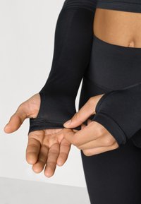 Haut de sport noir à manches longues avec trous pour les pouces, texture lisse, coupe ajustée et poignets sans coutures, complété par des leggings taille haute.