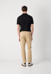 Zwart polo shirt met korte mouwen en een kraag, gecombineerd met khaki broeken. Sneakers hebben een zwart-wit kleurencombinatie.