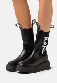 Black leather ankle boots with a chunky platform sole, featuring elastic sides and pull tabs. "KARL" logo in white on the side.