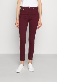 Jeans ajustados burdeos hechos de un material de algodón elástico con cierre de botón y cremallera, que presentan un diseño clásico de 5 bolsillos.