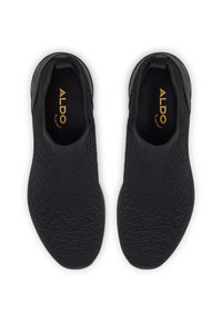 Chaussures noires sans lacets en matière tricotée texturée. Elles présentent un accent noir lisse au talon et un logo doré sur la semelle intérieure.