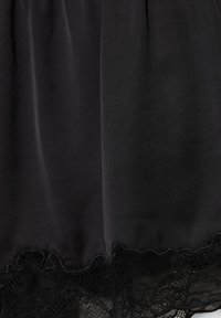 Tissu noir avec bordure en dentelle florale transparente en bas, montrant la texture et les détails délicats du motif.