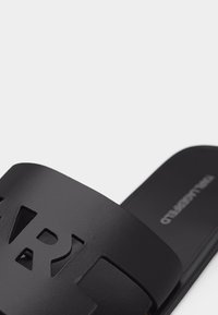 Μαύρη σαγιονάρα με φαρδιά λουρί που διαθέτει έντονα κομμένα γράμματα και επίπεδη σόλα.