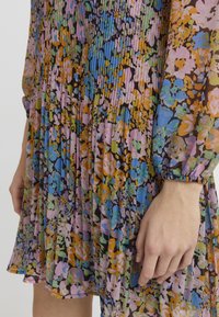 Daudzkrāsaina ziedu kleita ar krokām, caurspīdīgu audumu, garām piedurknēm un savilktu aproci. Dominējošas oranžas, rozā, zilas un zaļas krāsas.