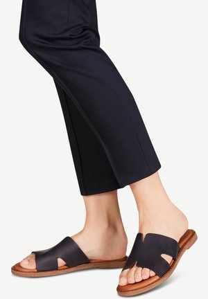 Sorte læder skydesandaler med udskåret design, tan sål og åben tå. Kombineret med korte navybukser.