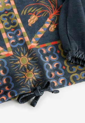 Tissu multicolore présentant des palmiers et des motifs géométriques. Fond sombre avec des accents décoratifs en rouge, jaune et bleu. Détail avec cordon de tirage.