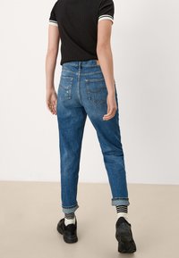 Modré džínové kalhoty s uvoln ěným střihem, ohrnutými nohavicemi, dvěma zadními kapsami a decentními švy. Nosí se s černou košilí a teniskami.