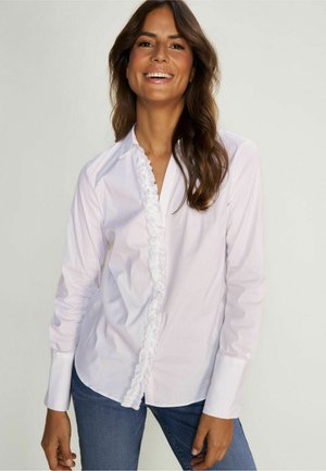 Camicia bianca con bottoni, caratterizzata da una parte anteriore arricciata, maniche lunghe e un colletto classico, abbinata a jeans blu. Tessuto morbido.