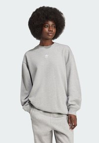 Grå oversize sweatshirt med rund hals, ribbede ærmer og blød tekstur. Har et lille hvidt logo på brystet. Sammen med matchende sweatpants.