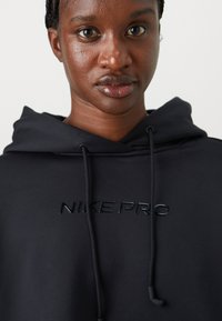 Svart Nike Pro hettegenser med en glatt tekstur, som har en hevet logo over brystet og justerbare snorer på hetta.