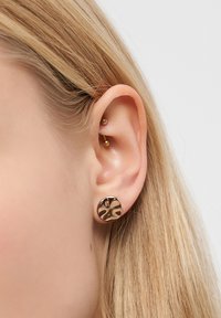 Nærbillede af et venstre øre med blont hår, iført en lille rund studs med skildpaddemønster og en guld barbells cartilage piercing.