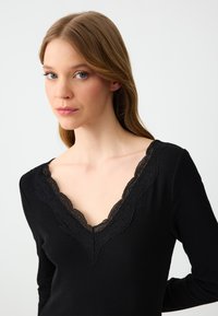 Schwarz gerippter Langarmtop mit V-Ausschnitt und detaillierter schwarzer Spitze. Glatte Textur und figurbetonte Passform.