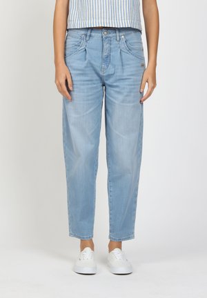 Person wearing light blue high-waist pleated jeans, striped sleeveless top, and white sneakers, standing against a plain white background.