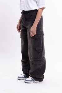 Pantalones cargo holgados y grises con múltiples bolsillos y detalles de broches. El material es de mezclilla con una textura suave, combinados con zapatillas azules y blancas.