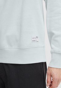 Lichtblauwe sweatshirt met ribgebreide boorden en zoom, voorzien van een klein wit stoffen label met tekst. Gladde textuur, casual pasvorm.