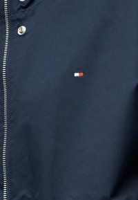 Μπλε ναυτικό μπουφάν με ασημένιο φερμουάρ και μικρό ορθογώνιο κόκκινο, άσπρο και μπλε λογότυπο στην περιοχή του στήθους.