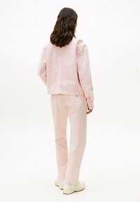Completo giacca in denim e pantaloni rosa chiaro, con un design corto, dettagli con bottoni e una vestibilità rilassata. Abbinato a sneaker in tonalità neutre.