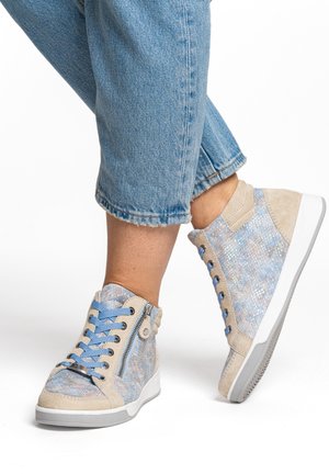 Feet wearing blue and beige patterned high-top sneakers with blue laces and side zippers, paired with cropped blue denim jeans.