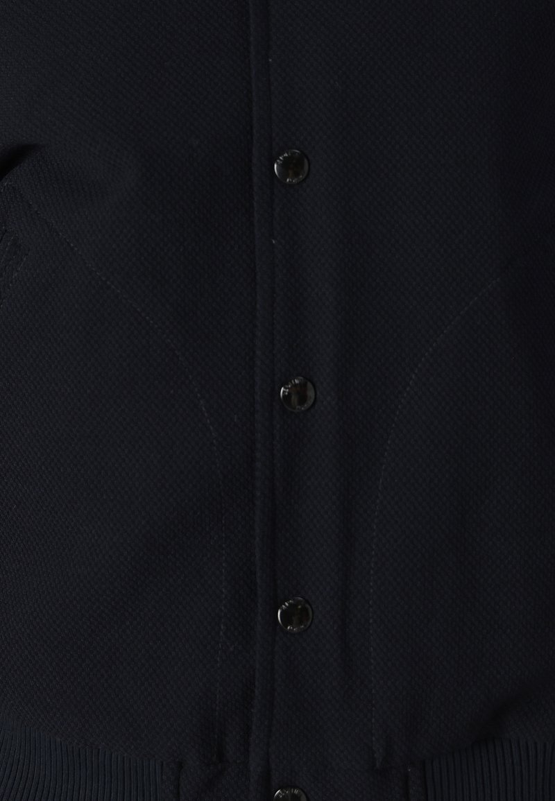 Cardigan a maglia blu navy con un motivo testurizzato, bottoni rotondi e polsini a coste. Il tessuto sembra morbido ed elastico.