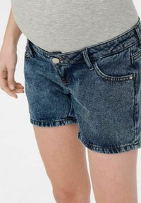 Jeans šortsevi u tamnoplavoj boji s blagim izbljeđivanjem, dizajn s pet džepova i uvijenim rubom. Imaju metalni gumb i petlje za remen.