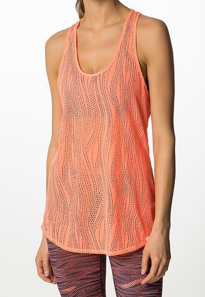 Femme portant un débardeur corail en maille sans manches avec un motif ondulé à points et des leggings à motifs sur fond blanc.