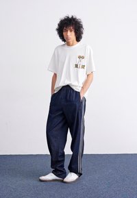 White t-shirt with a cactus graphic, paired with dark blue athletic pants featuring side stripes and white sneakers.